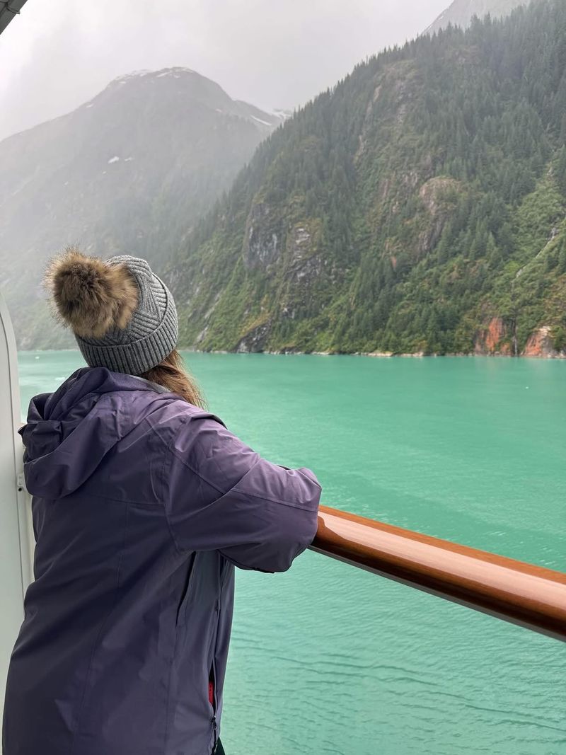 ’Chelle at a ship’s rail, looking out over a green fjord and forested mountains