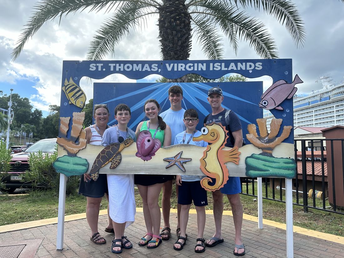 ’Chelle and her family posing at a colorful St. Thomas, Virgin Islands sign, with a cruise ship behind
