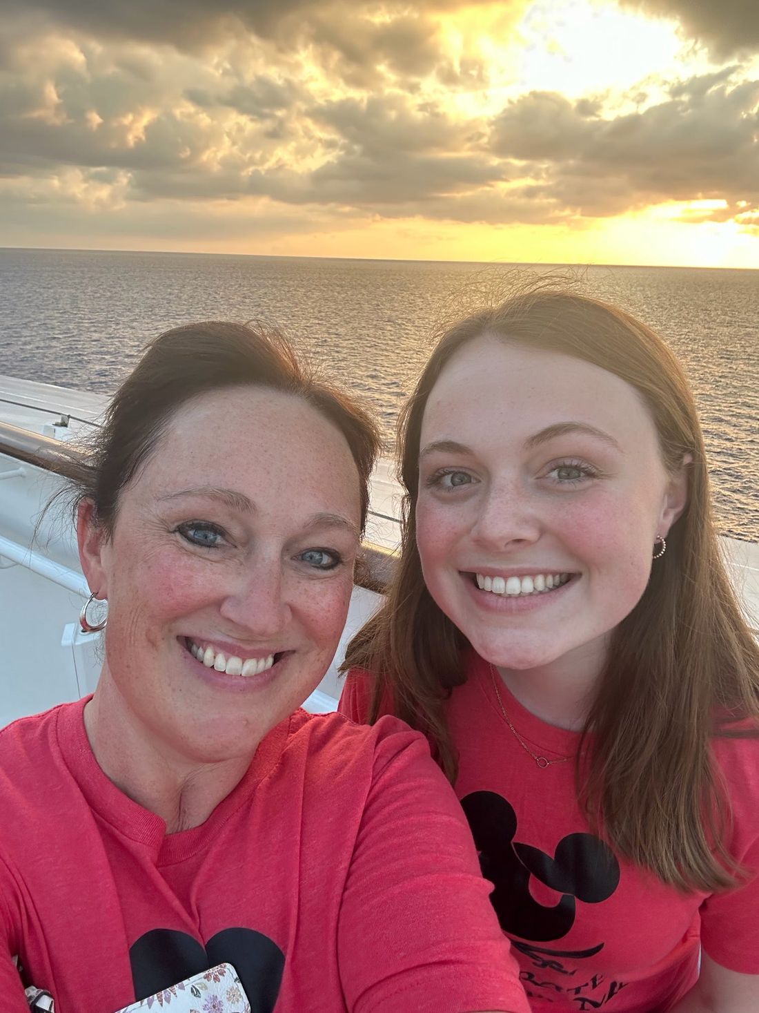 ’Chelle and her daughter in Mickey shirts smiling on a Disney cruise ship deck at sunset