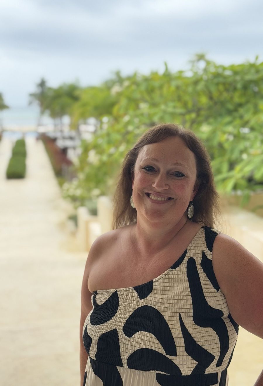 ’Chelle smiling on a sunny walkway lined with greenery