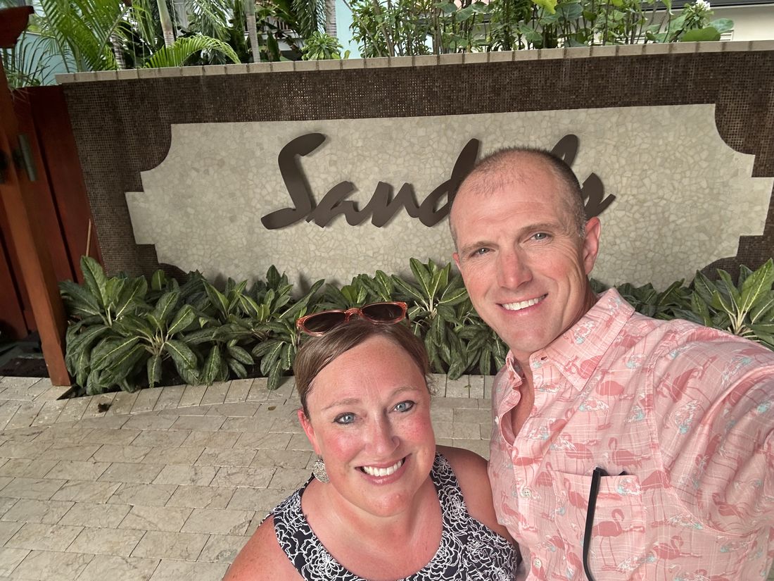 ’Chelle and her husband, Jeremy, smiling in front of a Sandals resort sign